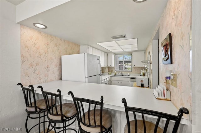 kitchen featuring sink, kitchen peninsula, white appliances, a kitchen bar, and white cabinets