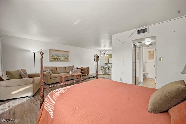 bedroom featuring connected bathroom, light hardwood / wood-style floors, and a notable chandelier