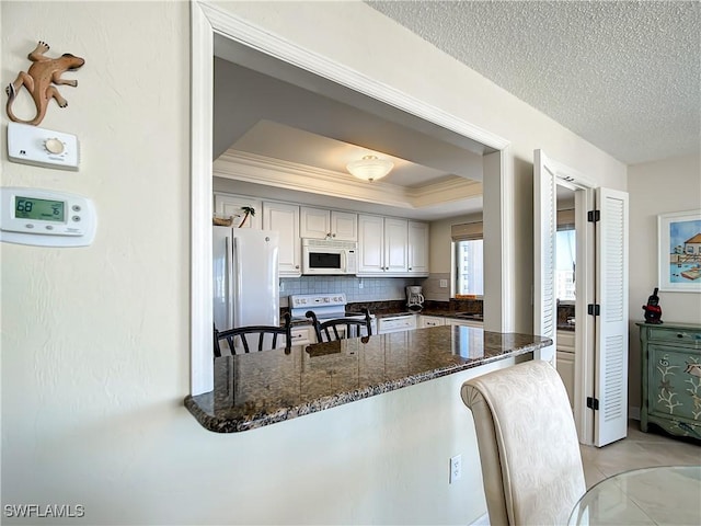 kitchen with white appliances, dark stone countertops, a textured ceiling, tasteful backsplash, and kitchen peninsula