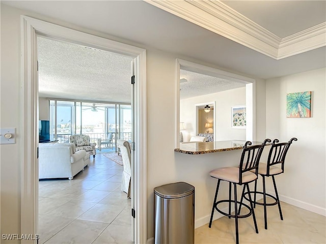 kitchen with a breakfast bar, crown molding, ceiling fan, stone countertops, and a wall of windows