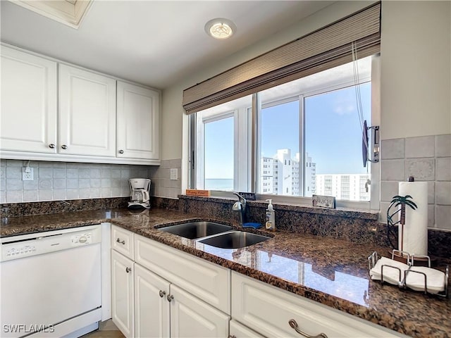 kitchen with a wealth of natural light, sink, dark stone countertops, dishwasher, and white cabinetry