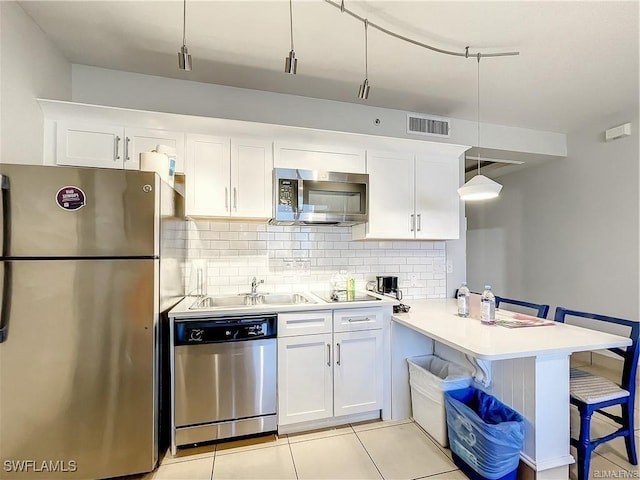 kitchen featuring kitchen peninsula, appliances with stainless steel finishes, decorative light fixtures, a kitchen bar, and white cabinetry