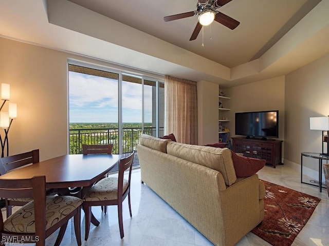 living room featuring built in shelves, a raised ceiling, and ceiling fan