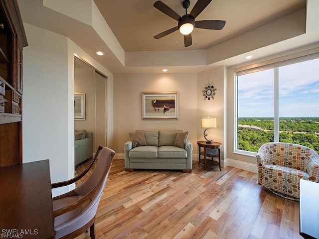 living room featuring ceiling fan, light hardwood / wood-style floors, a raised ceiling, and a wealth of natural light