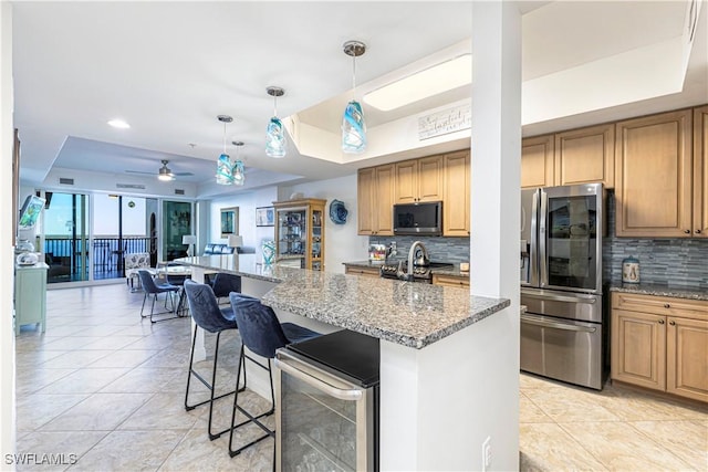 kitchen with a breakfast bar, stainless steel appliances, a tray ceiling, ceiling fan, and wine cooler