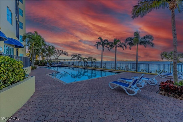 pool at dusk featuring a patio area and a water view