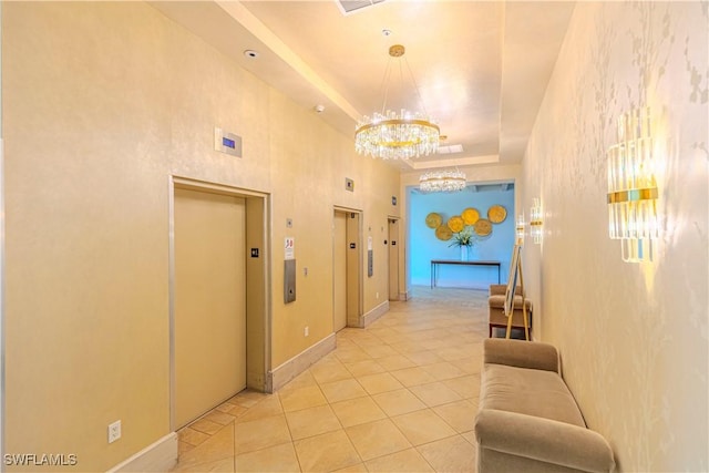 corridor with a tray ceiling, elevator, light tile patterned floors, and an inviting chandelier