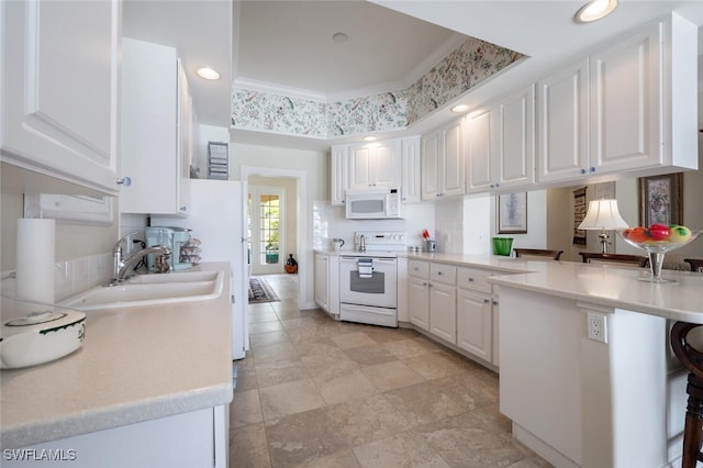 kitchen featuring a breakfast bar, white appliances, white cabinets, sink, and kitchen peninsula