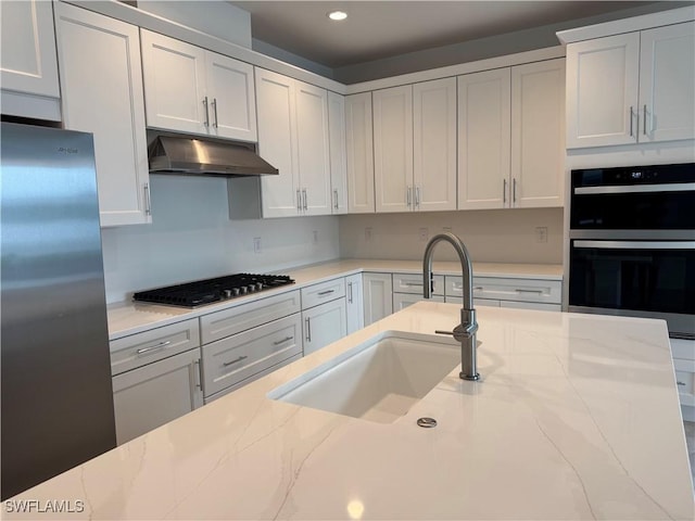 kitchen with double oven, under cabinet range hood, a sink, gas stovetop, and freestanding refrigerator