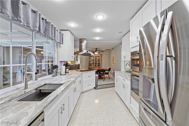 kitchen with white cabinetry, sink, light stone countertops, stainless steel appliances, and island range hood