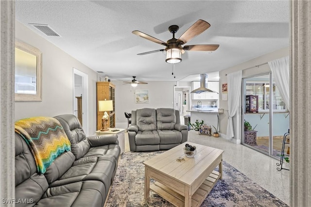 living room with ceiling fan, sink, and a textured ceiling