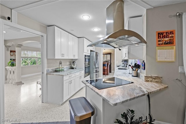 kitchen with white cabinetry, ornate columns, island range hood, kitchen peninsula, and stainless steel appliances