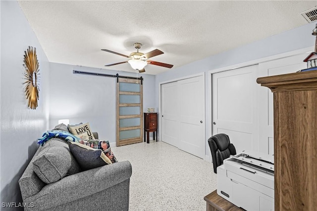 home office featuring a textured ceiling, a barn door, and ceiling fan