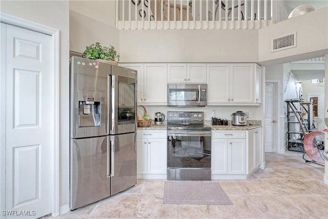 kitchen with white cabinets, light stone counters, a high ceiling, and appliances with stainless steel finishes