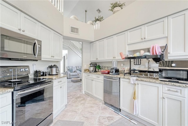 kitchen featuring white cabinets, a high ceiling, stainless steel appliances, and light stone counters