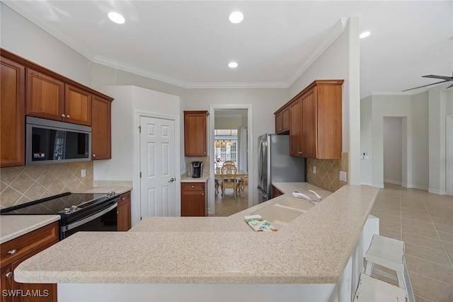 kitchen featuring kitchen peninsula, crown molding, a breakfast bar area, decorative backsplash, and appliances with stainless steel finishes