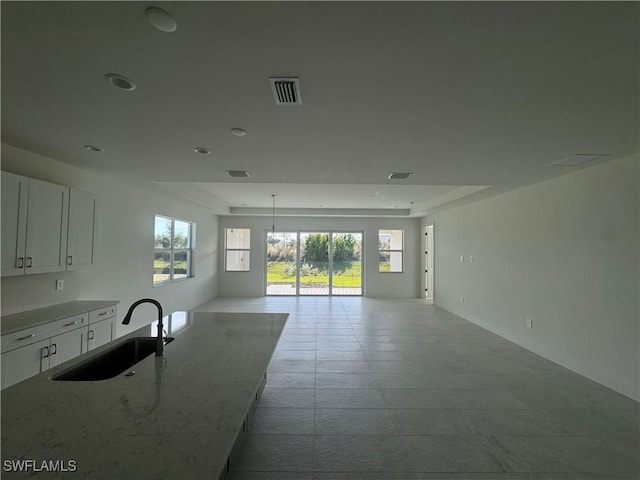 interior space featuring a raised ceiling, light stone counters, sink, and white cabinets