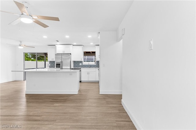 kitchen with white cabinets, stainless steel fridge, light wood-type flooring, and tasteful backsplash