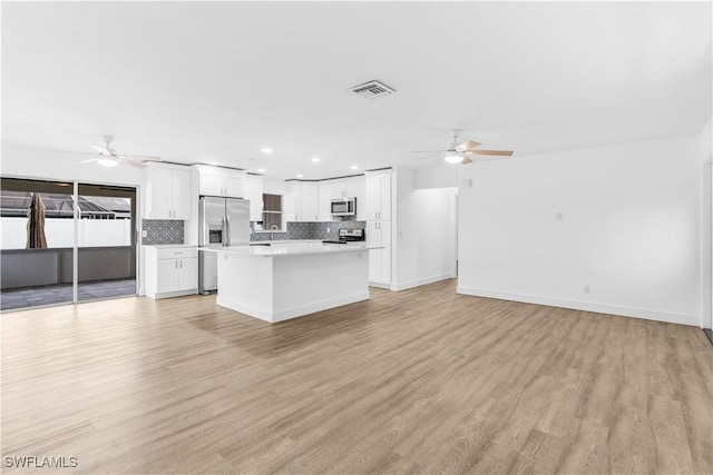 kitchen featuring white cabinets, appliances with stainless steel finishes, light hardwood / wood-style floors, and decorative backsplash