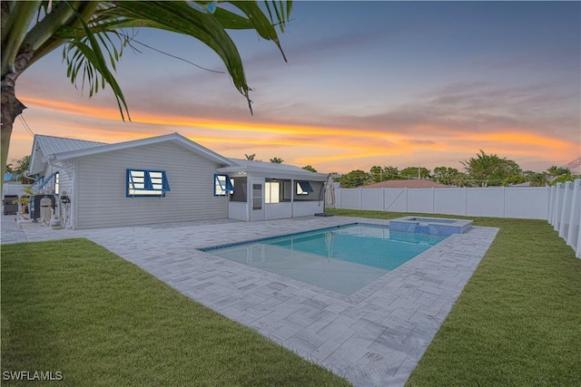 pool at dusk featuring a patio area, a yard, and an in ground hot tub