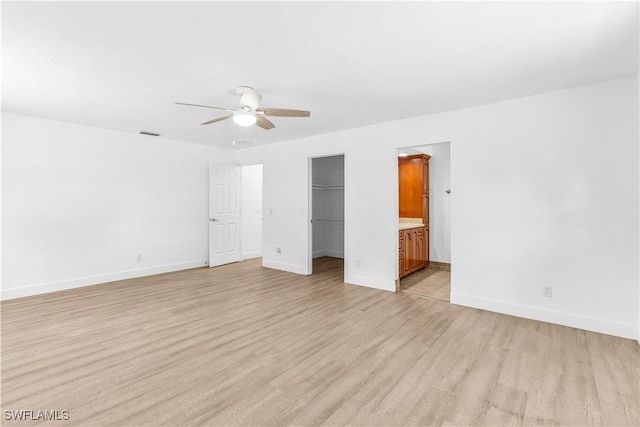 unfurnished bedroom with ensuite bathroom, ceiling fan, a spacious closet, light hardwood / wood-style floors, and a closet