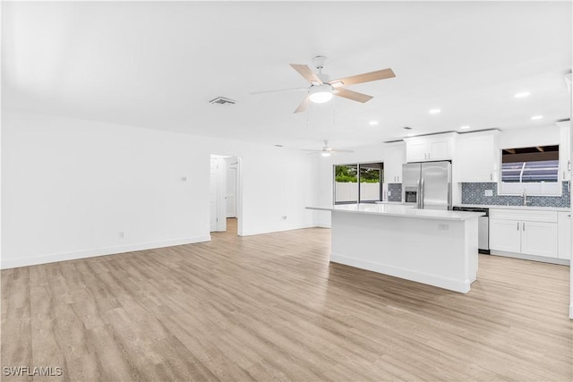 kitchen with appliances with stainless steel finishes, tasteful backsplash, light hardwood / wood-style flooring, white cabinets, and a center island