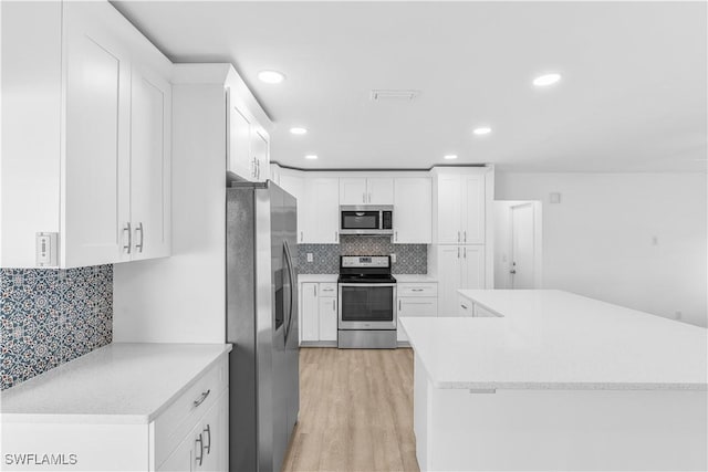 kitchen featuring tasteful backsplash, kitchen peninsula, light hardwood / wood-style floors, white cabinets, and appliances with stainless steel finishes