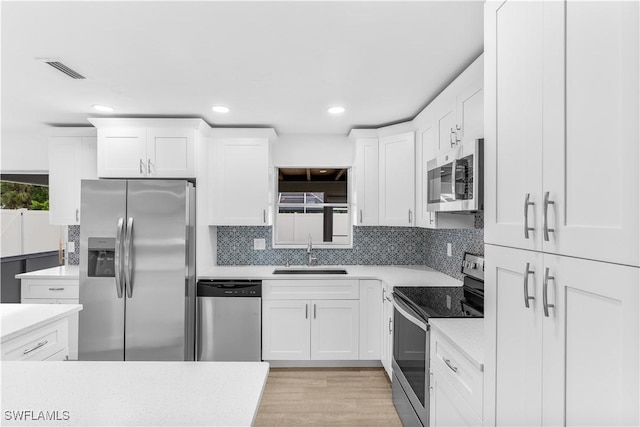 kitchen with sink, tasteful backsplash, light hardwood / wood-style floors, white cabinets, and appliances with stainless steel finishes