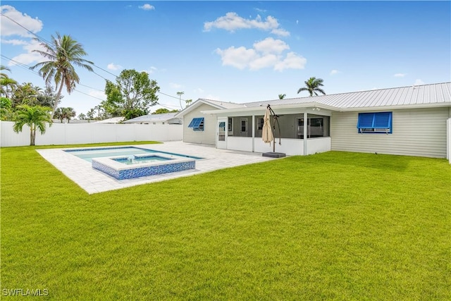 back of property featuring a sunroom, a patio area, an in ground hot tub, and a lawn