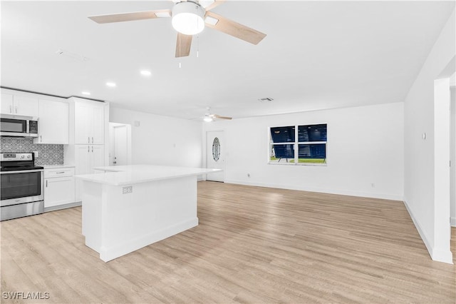 kitchen with decorative backsplash, appliances with stainless steel finishes, light wood-type flooring, white cabinets, and a center island