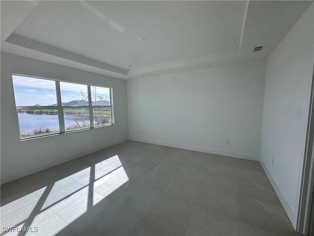 tiled empty room featuring a raised ceiling and a water view