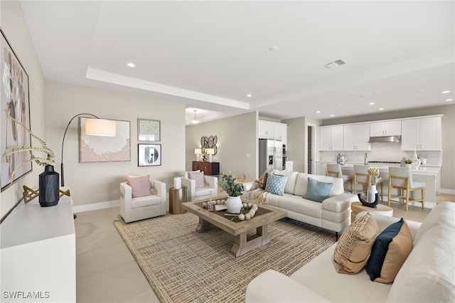 living area featuring light tile patterned flooring, visible vents, baseboards, recessed lighting, and a tray ceiling