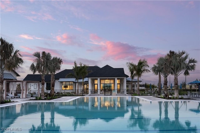 pool at dusk with fence, a patio, and a community pool