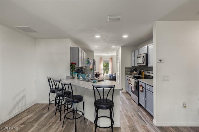 kitchen with a kitchen bar, kitchen peninsula, stainless steel appliances, and light wood-type flooring