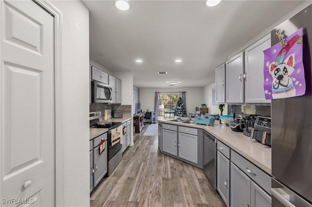 kitchen featuring gray cabinetry, backsplash, sink, appliances with stainless steel finishes, and light hardwood / wood-style floors