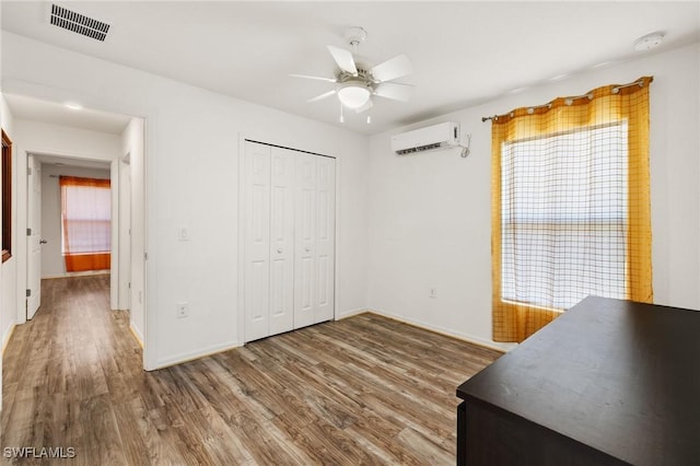 bedroom featuring a wall mounted air conditioner, hardwood / wood-style floors, a closet, and ceiling fan