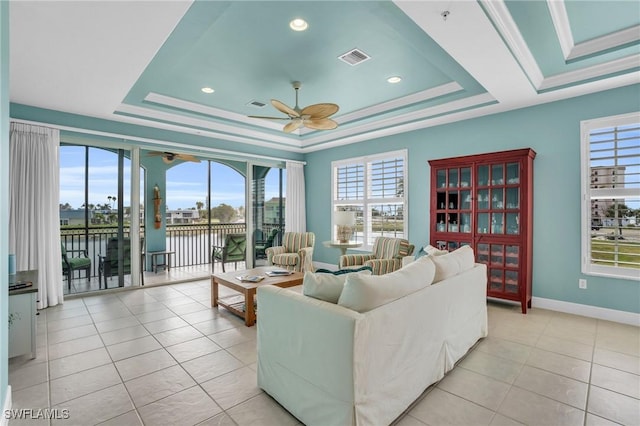 living room featuring a tray ceiling, crown molding, a water view, and light tile patterned floors