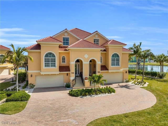 mediterranean / spanish home with a front lawn, a water view, and a garage