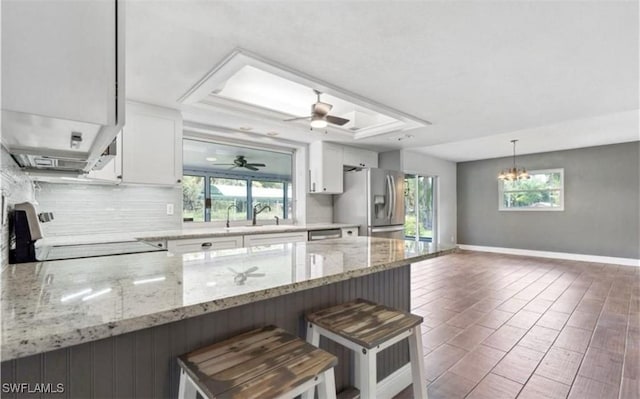 kitchen with range, a raised ceiling, white cabinets, stainless steel fridge with ice dispenser, and a breakfast bar area