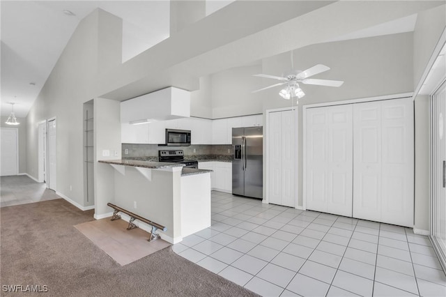 kitchen featuring kitchen peninsula, light tile patterned floors, a towering ceiling, appliances with stainless steel finishes, and white cabinetry