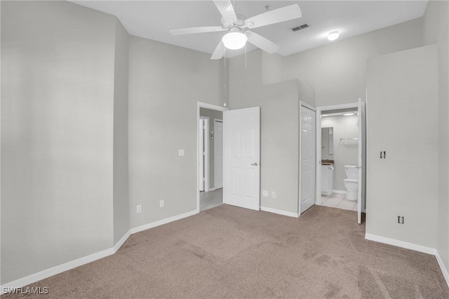 unfurnished bedroom featuring ceiling fan, light colored carpet, a high ceiling, and ensuite bath