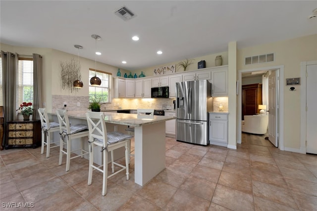 kitchen with light stone countertops, stainless steel fridge, decorative light fixtures, white cabinets, and a breakfast bar area