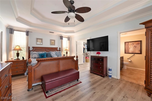 bedroom featuring ceiling fan, ensuite bathroom, ornamental molding, light hardwood / wood-style floors, and a raised ceiling