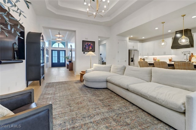 living room featuring french doors, a towering ceiling, a tray ceiling, a notable chandelier, and light hardwood / wood-style floors