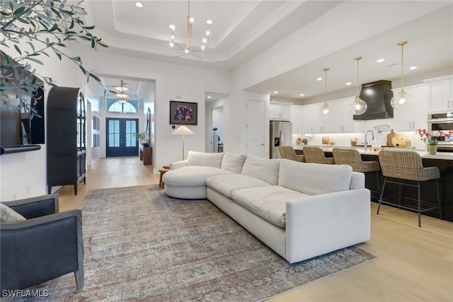 living room with sink, a notable chandelier, a towering ceiling, a tray ceiling, and light wood-type flooring