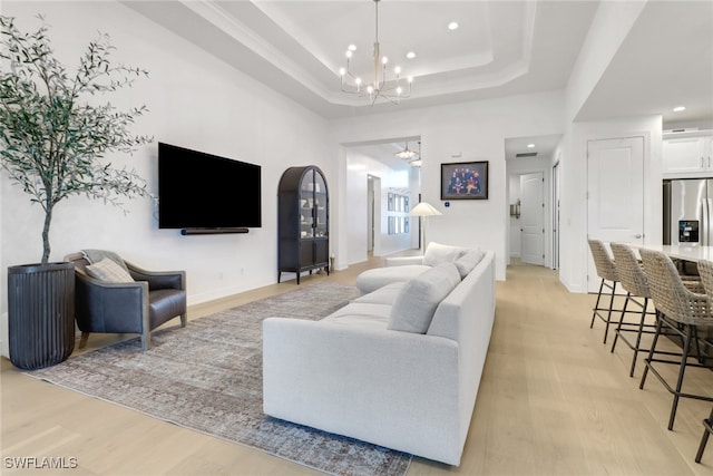 living room with light wood-type flooring, a tray ceiling, and a notable chandelier