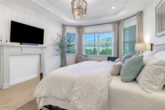 bedroom featuring light wood-type flooring, a tray ceiling, an inviting chandelier, and ornamental molding