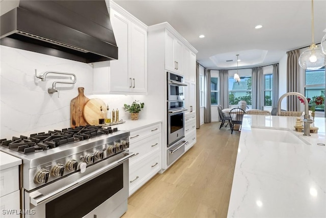 kitchen with custom range hood, stainless steel appliances, hanging light fixtures, and sink