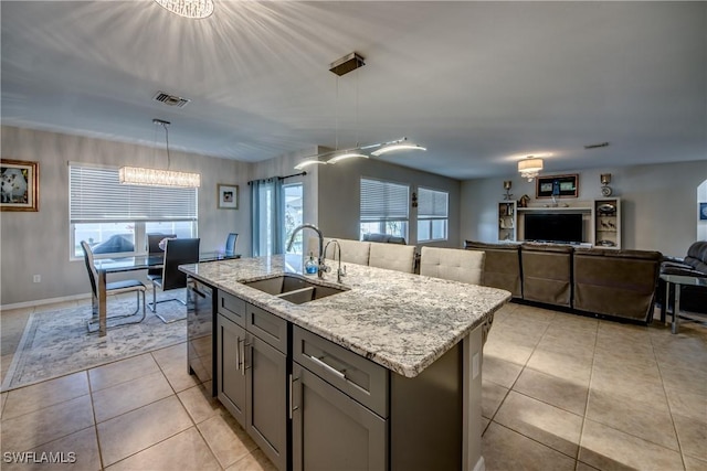 kitchen with pendant lighting, a kitchen island with sink, sink, light stone countertops, and a chandelier