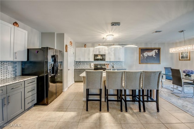 kitchen featuring hanging light fixtures, light stone counters, an island with sink, light tile patterned flooring, and black appliances